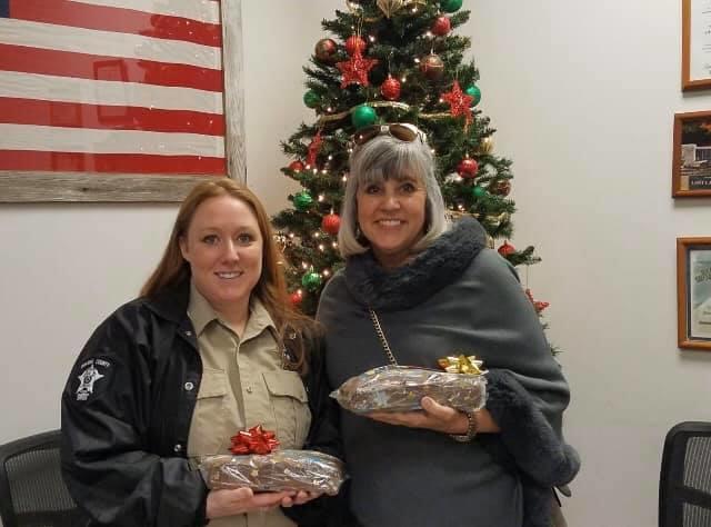 female deputy and citizen holding donated holiday treats in front of a Christmas tree