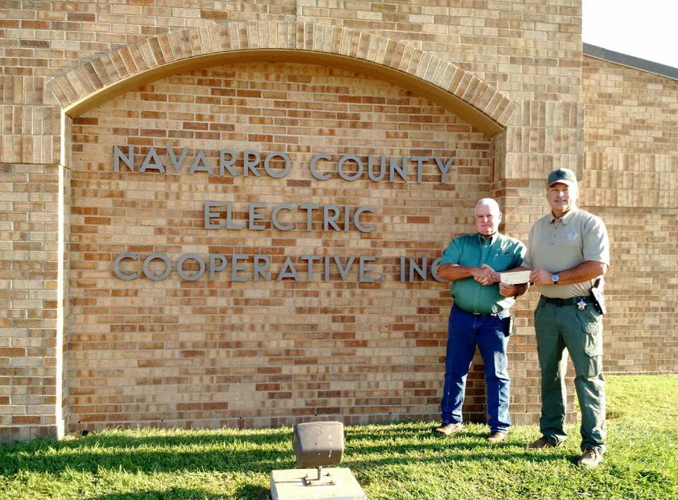 Sheriff Tanner shakes hands and accepts a check in front of the Navarro County Electric Cooperative Inc