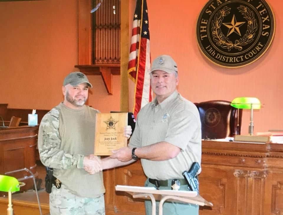 Two Navarro County officers shake hands and exchange an award