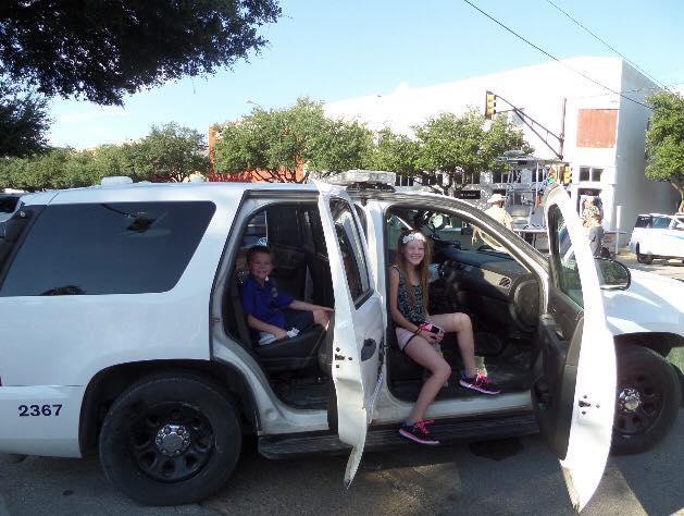 Two children pose inside of a police vehicle