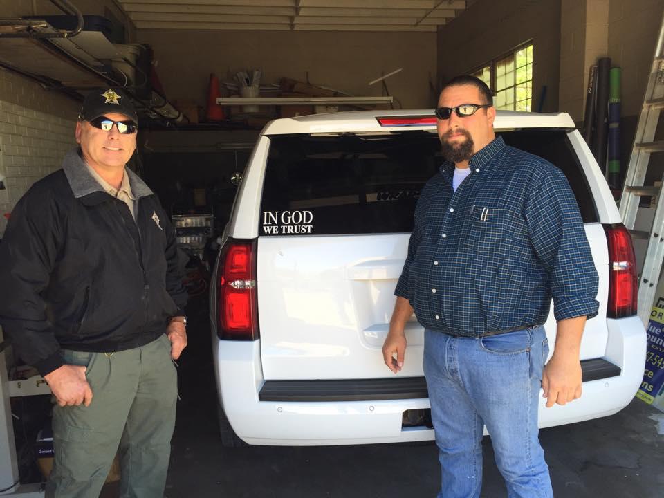 Sheriff Tanner and other stand next to a Tahoe with a new "In God We Trust" decal