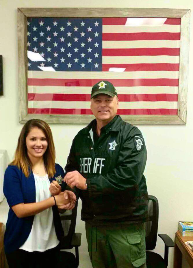 Emilia Ramires shakes Sheriff Tanner's hand as he hands her a sheriff badge