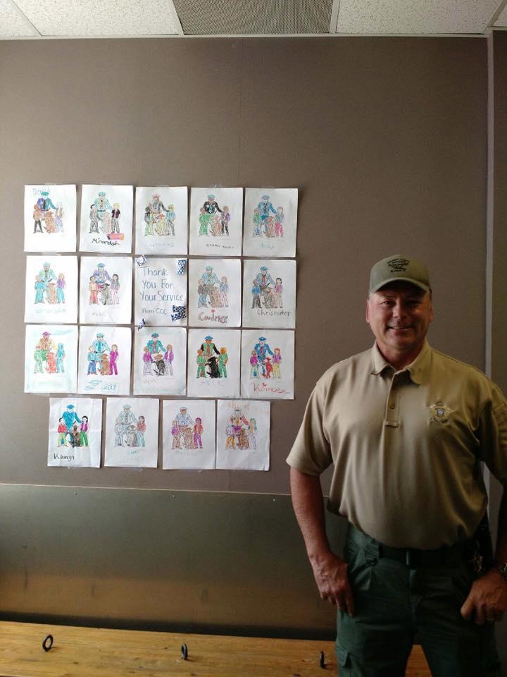 Sheriff Tanner smiles and stands next to some coloring pages 