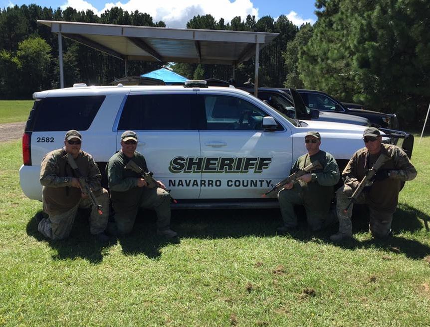 Brandon Bates, Keith Lewis, Sgt. Robbie Jock and Sgt. Jeff Harbuck kneel in front of a Navarro County Sheriff's vehicle